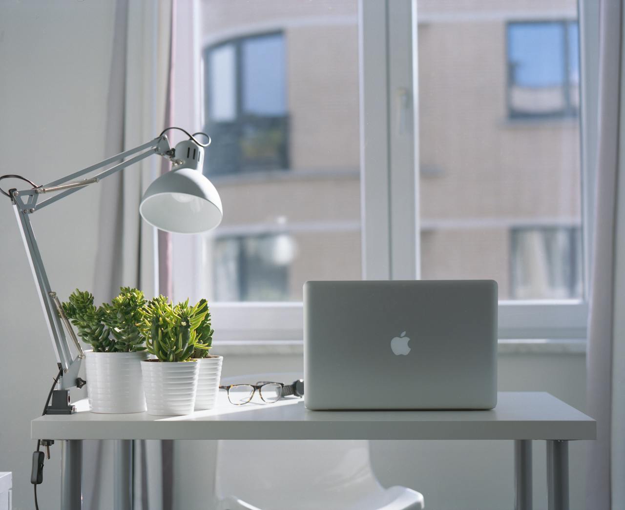 journey Bright modern workspace with laptop, potted plants, and desk lamp near a window.